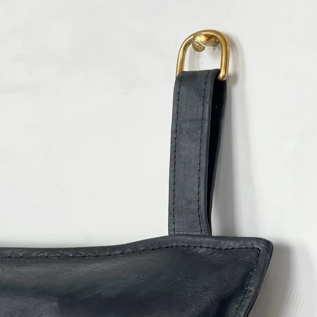 Close-up of a black leather headboard strap looped over a brass wall hook