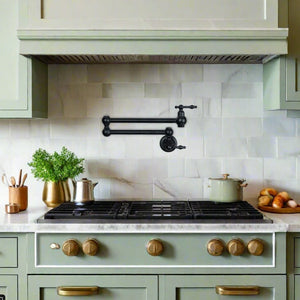 Black retractable pot filler mounted over a kitchen range with green cabinetry and marble backsplash, blending function and traditional style