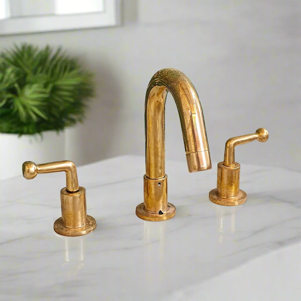 Three-hole widespread bathroom faucet with aged brass finish and modern lever handles, installed on a white marble countertop