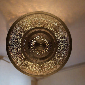 Close-up view of the underside of a handcrafted Moroccan brass ceiling lamp, highlighting the detailed hand-punched patterns that create decorative shadow effects