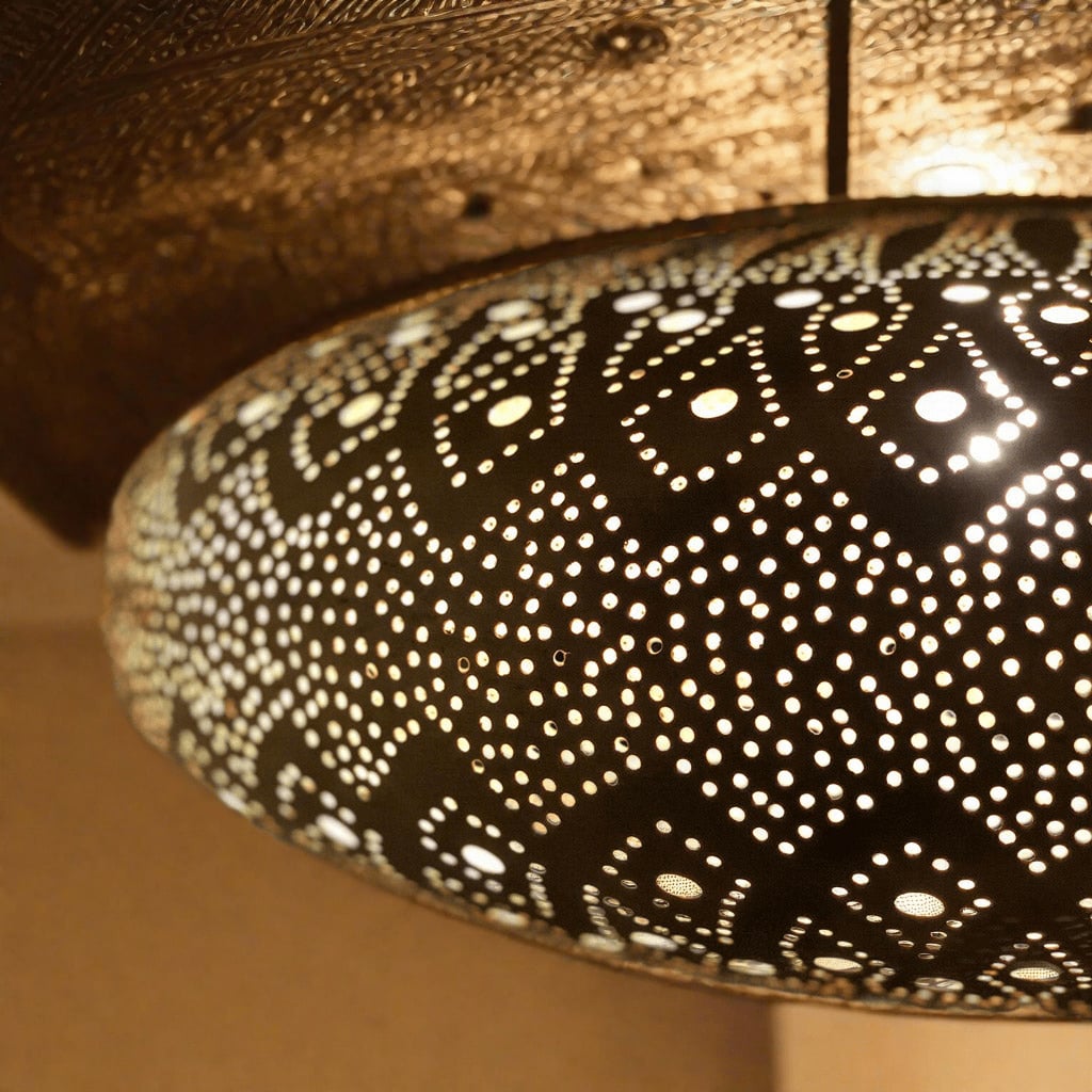 Close-up of a Moroccan light fixture showcasing intricate brass perforations and traditional design elements, casting a warm, ambient glow on the wall