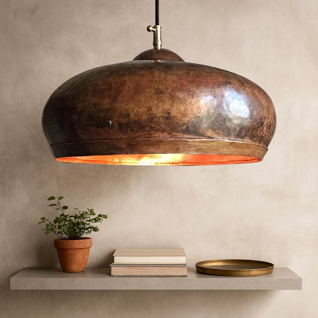Moroccan hammered copper pendant light turned on, casting a warm glow onto the floating shelf below with books and simple decor