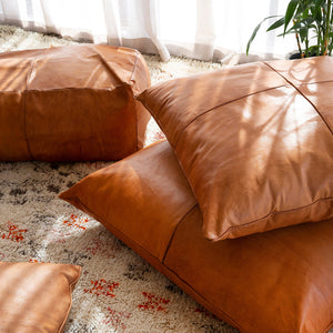 Handcrafted custom leather pillows in tan and light tan, displayed on a rug with natural light.