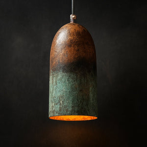 Handcrafted Moroccan pendant light with an elongated organic dome shape, featuring a unique ombré patina blending rich copper and oxidized green tones, and a warm glowing interior, set against a dark background