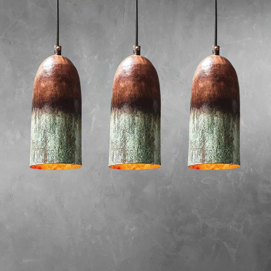 Set of three handcrafted Moroccan pendant lights with tall, rounded organic shapes, featuring a rich ombré patina blending earthy brown and green tones, and glowing golden interiors, suspended against a textured gray wall