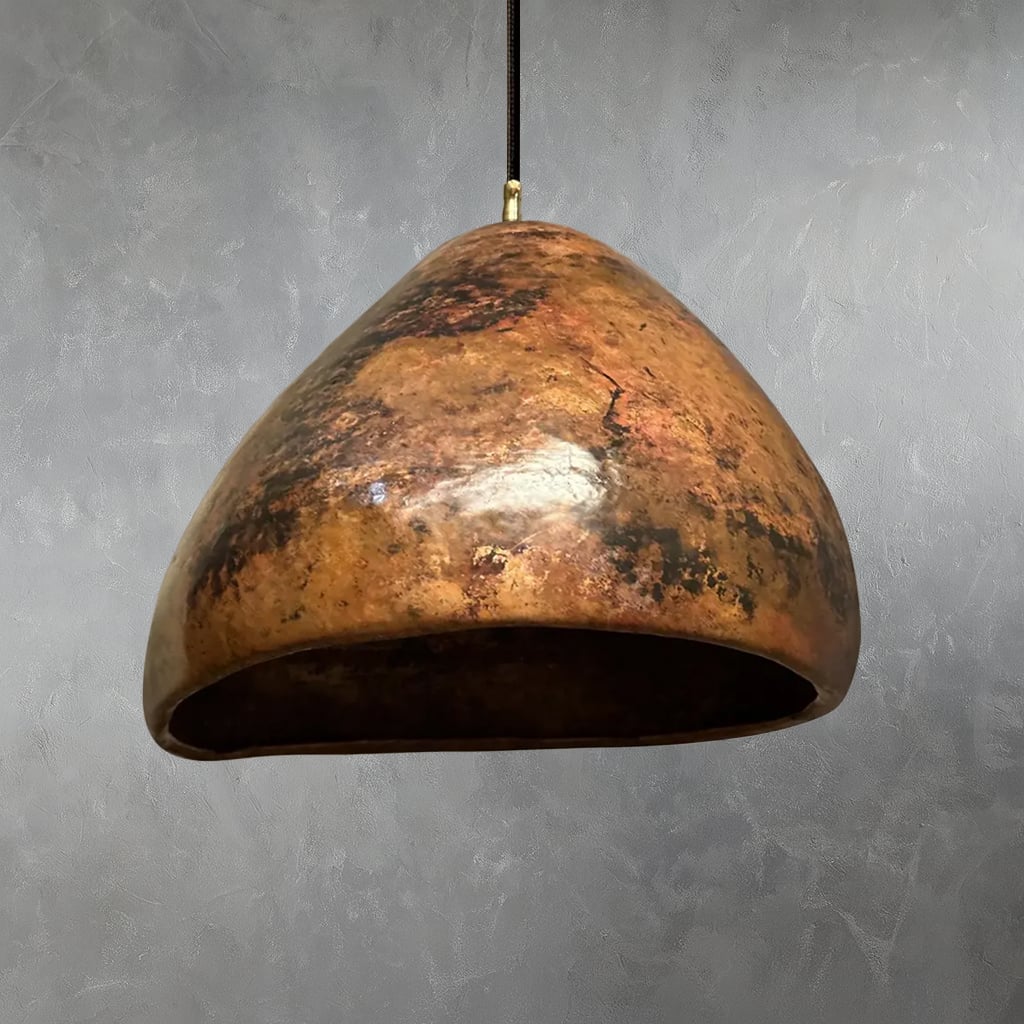Handcrafted Moroccan pendant light with an organic dome shape, featuring a richly patinated hammered copper surface and artisanal texture, suspended against a gray textured wall