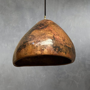 Handcrafted Moroccan pendant light with an organic dome shape, featuring a richly patinated hammered copper surface and artisanal texture, suspended against a gray textured wall