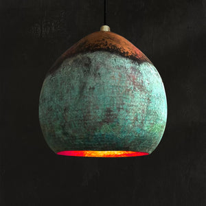 Handcrafted Moroccan pendant light with a rounded organic silhouette, featuring a striking ombré patina in copper and oxidized green, glowing with warm light against a dark background