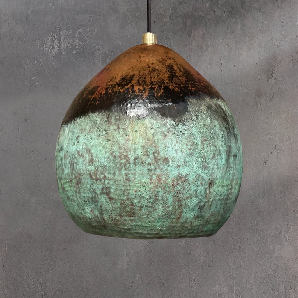 Handcrafted Moroccan pendant light with a rounded organic shape, featuring a unique ombré patina blending warm copper and oxidized green tones, suspended against a textured gray wall