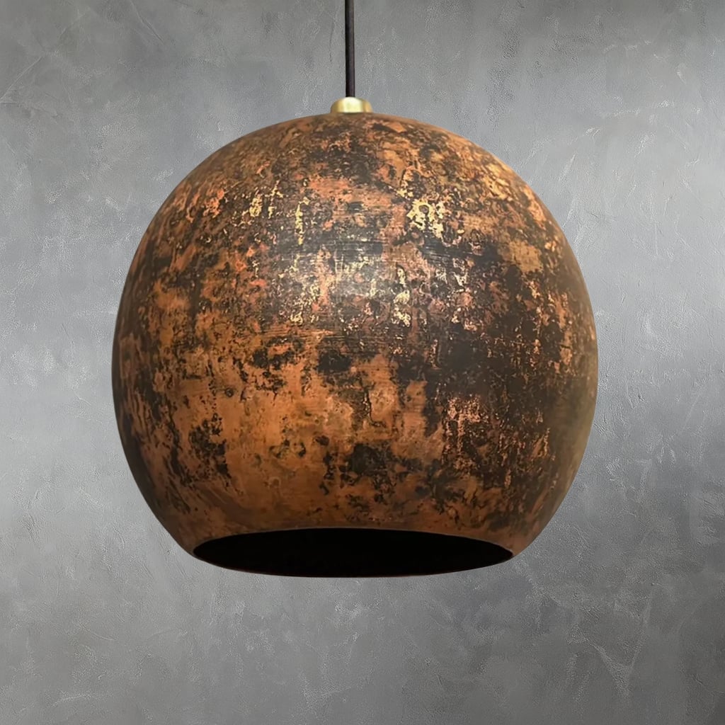 Handcrafted Moroccan pendant light with a rounded organic silhouette, featuring a dark, distressed hammered copper finish, suspended against a textured gray wall for a rustic-modern look