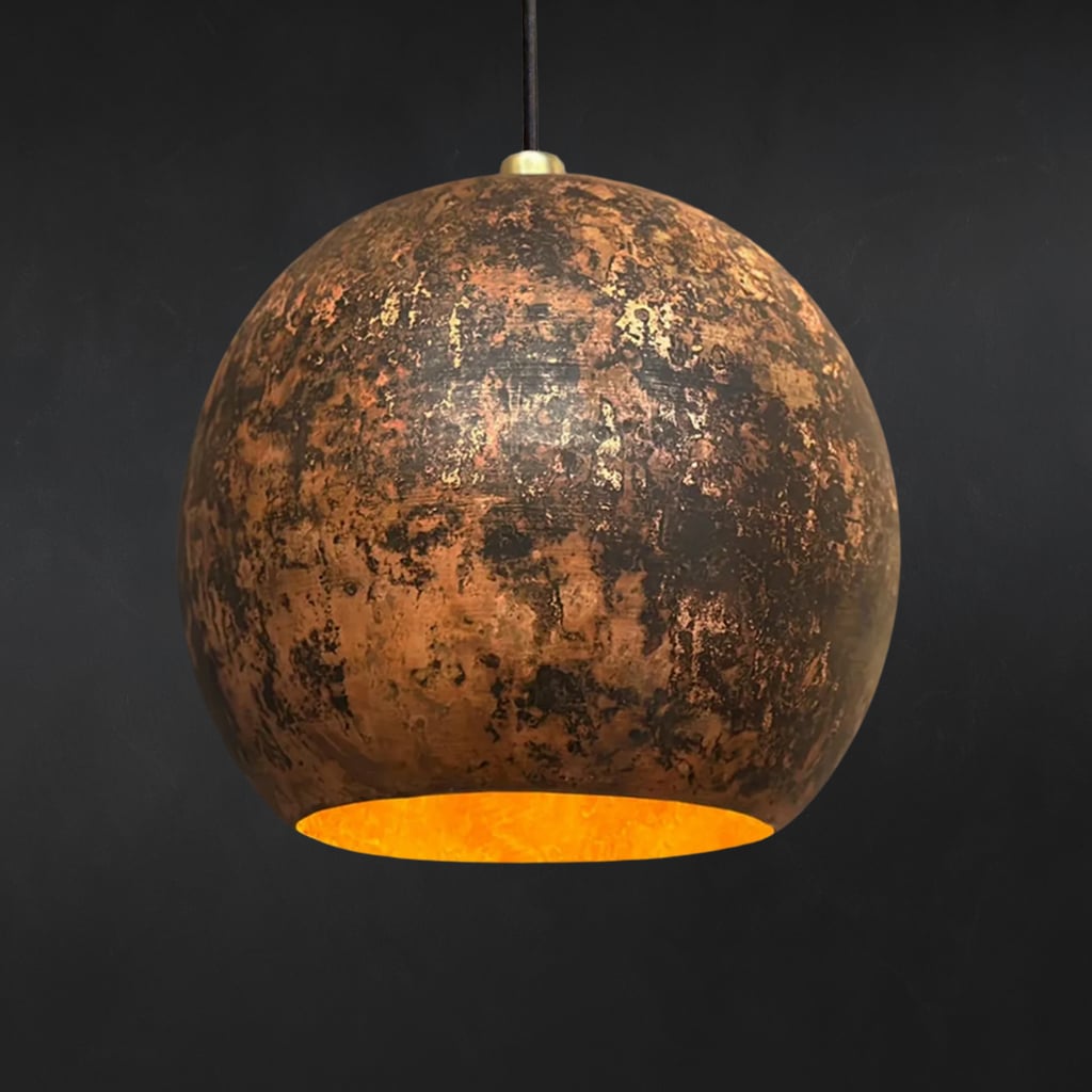 Handcrafted Moroccan pendant light with a rounded organic shape, featuring a dark, richly patinated hammered copper finish and a glowing golden interior, suspended against a black background