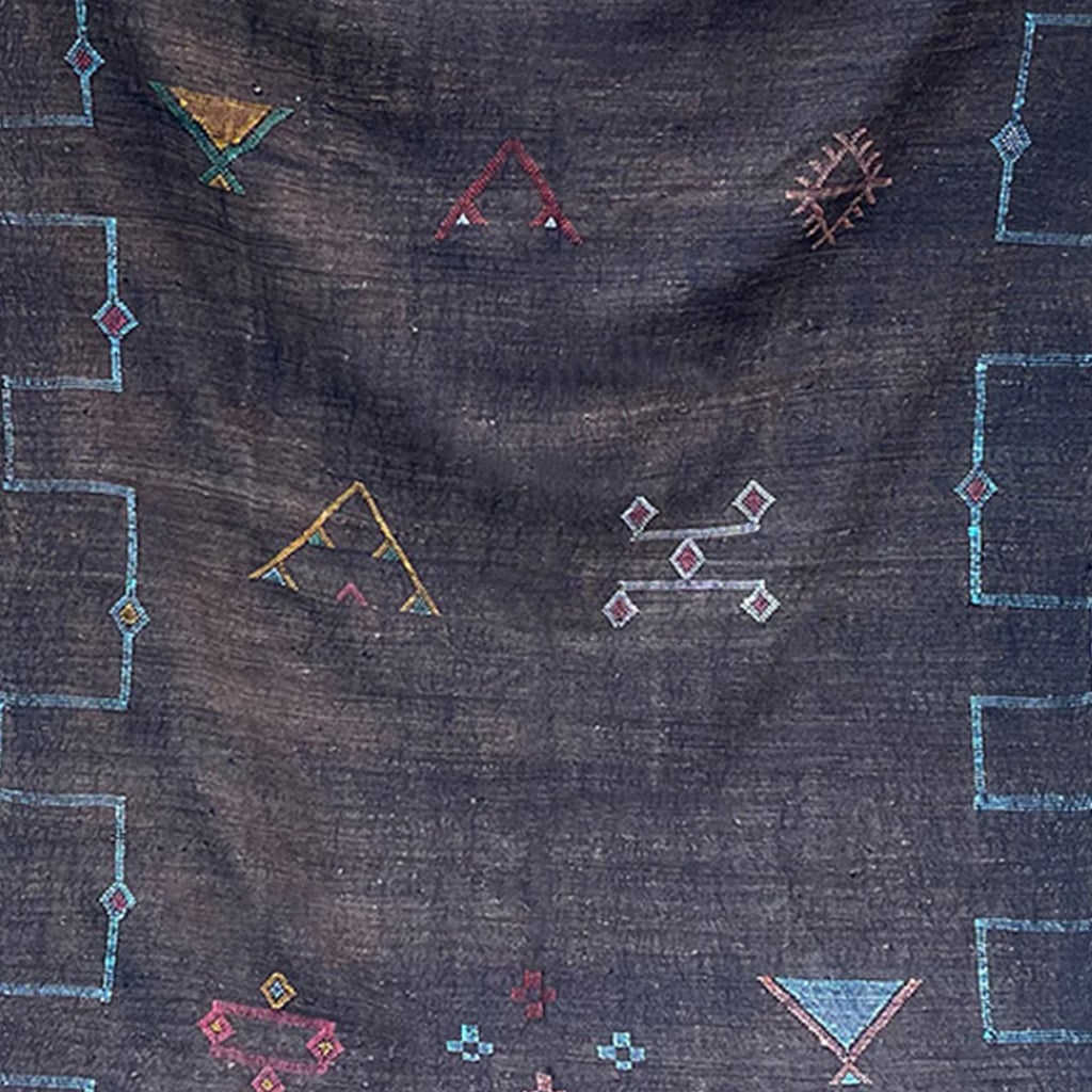 Close-up of a black Moroccan sabra cactus silk rug with colorful geometric Berber motifs and embroidered tribal symbols