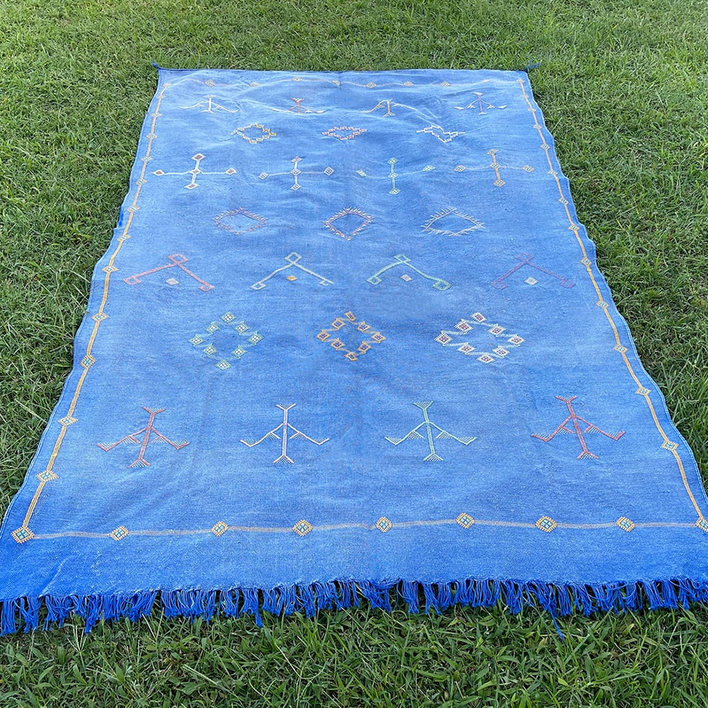 Handwoven blue Moroccan sabra cactus silk rug with traditional Berber motifs and fringe edges, displayed outdoors on grass