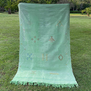Handwoven Moroccan sabra cactus silk rug in soft mint green, adorned with subtle embroidered geometric and tribal motifs, finished with fringed edges