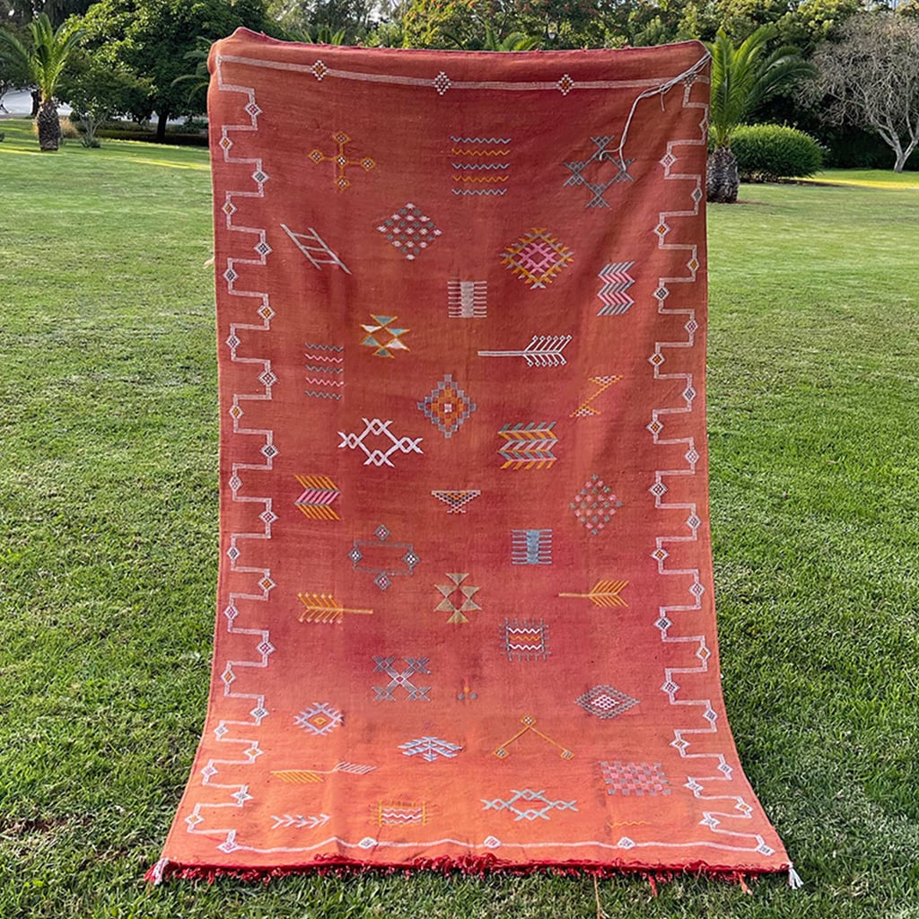 Handwoven Moroccan sabra cactus silk rug in terracotta orange, featuring colorful geometric and arrow motifs with white embroidered border details