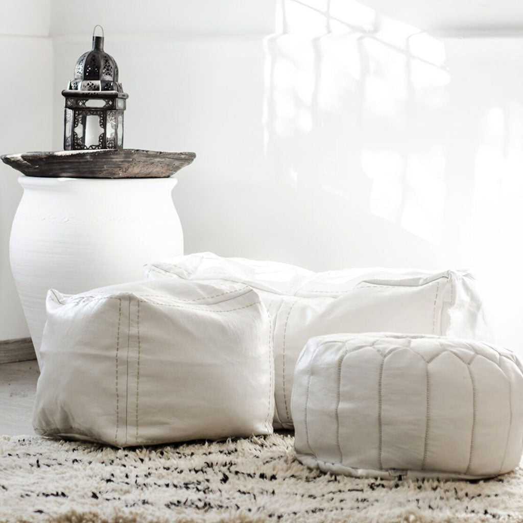 Bright room with bunch of Moroccan white leather poufs on black and white Berber rug, beside handmade white clay decoration - Moroccan Interior