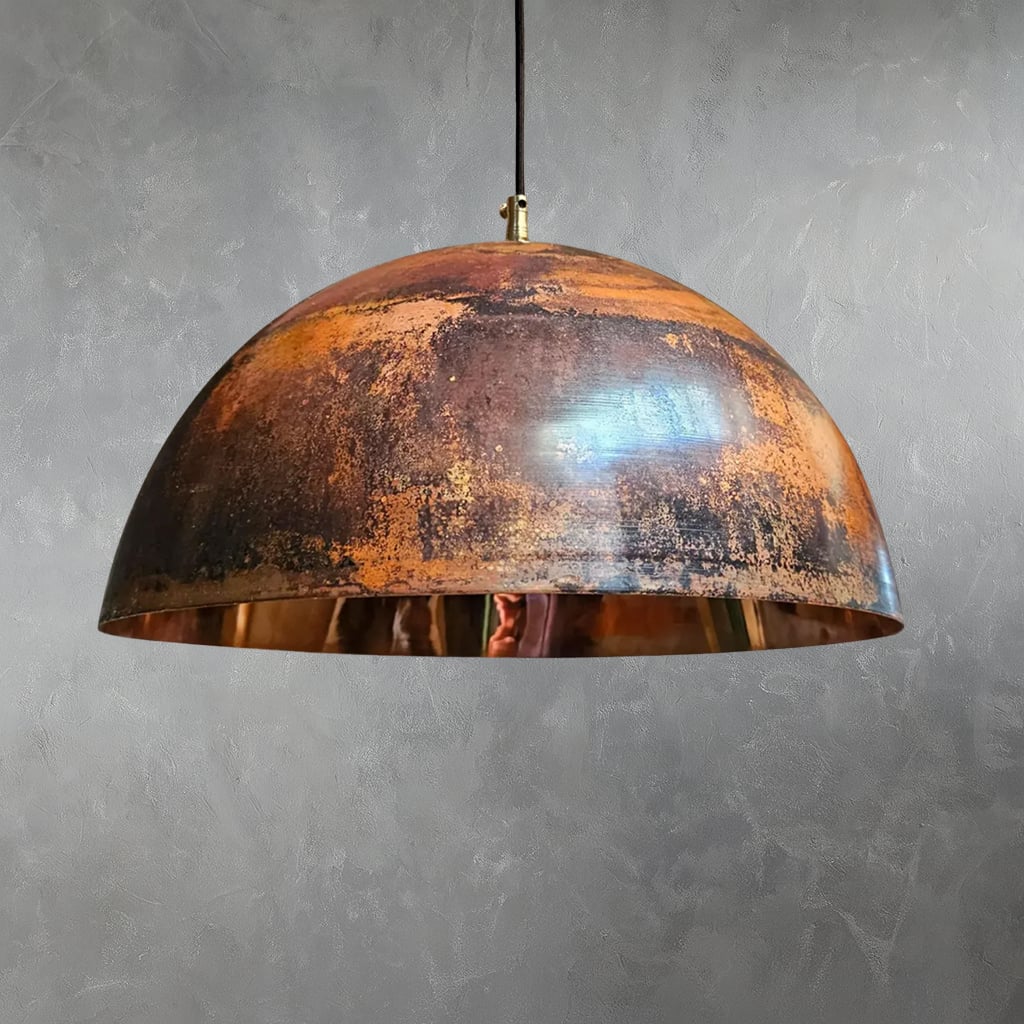 Handcrafted Moroccan pendant light with a wide dome shape, featuring a richly textured patina in warm copper and dark tones, suspended against a gray textured wall