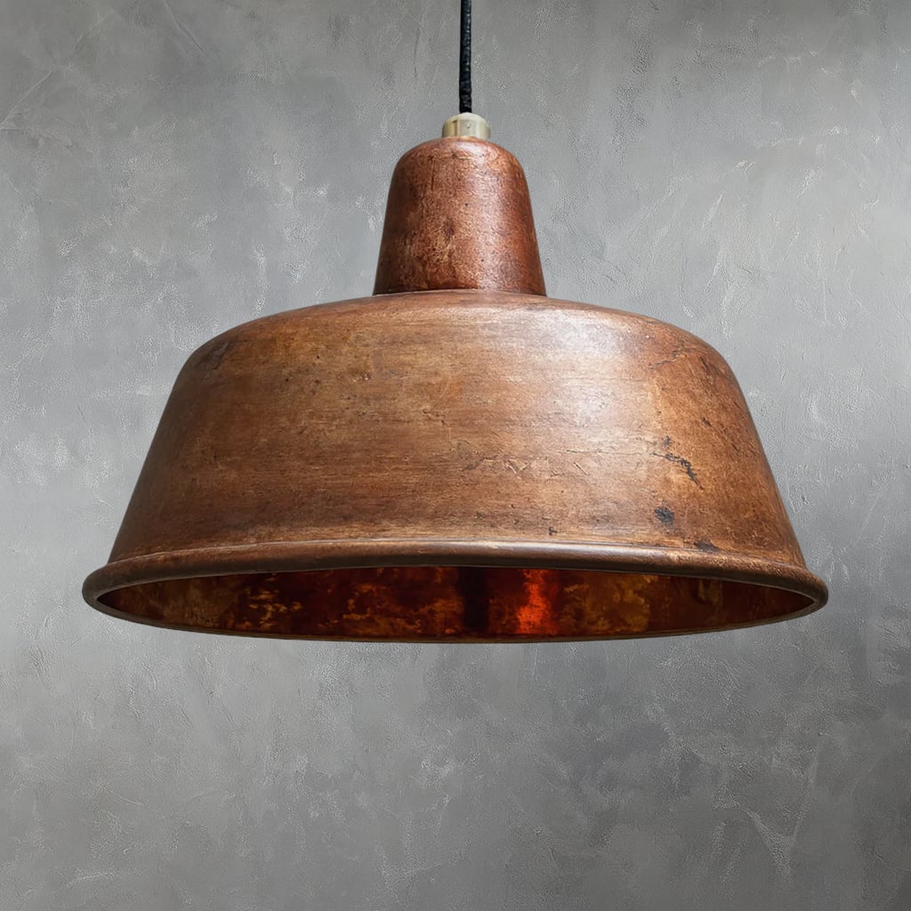 Handcrafted Moroccan pendant light with a wide, flared shade made from hammered copper, featuring a warm, rustic patina and suspended against a textured gray wall