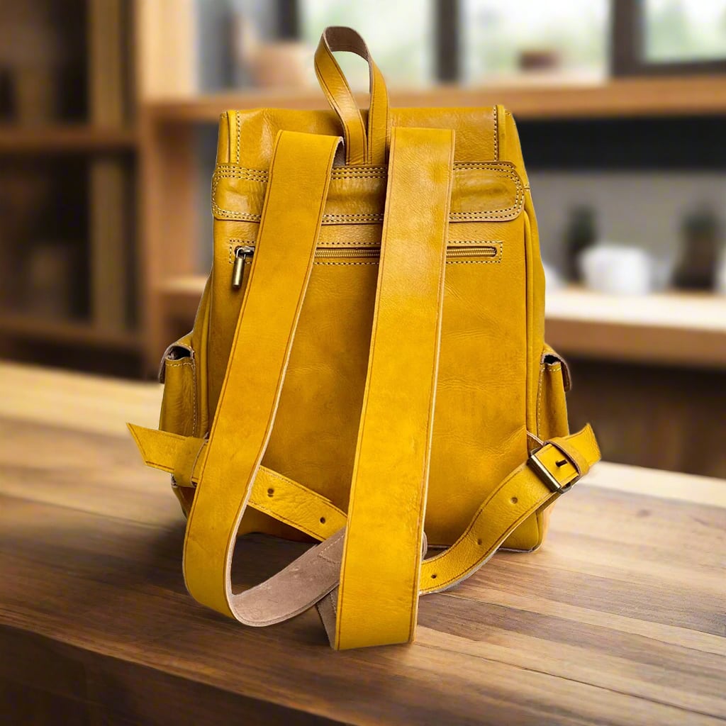 Back view of a yellow Moroccan leather backpack with adjustable straps and a zippered pocket, set on a wooden table in a warmly lit room with shelves and neutral decor