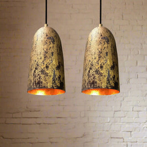 Pair of oxidized copper bell pendant lights with warm inner glow, hanging in front of a white brick wall