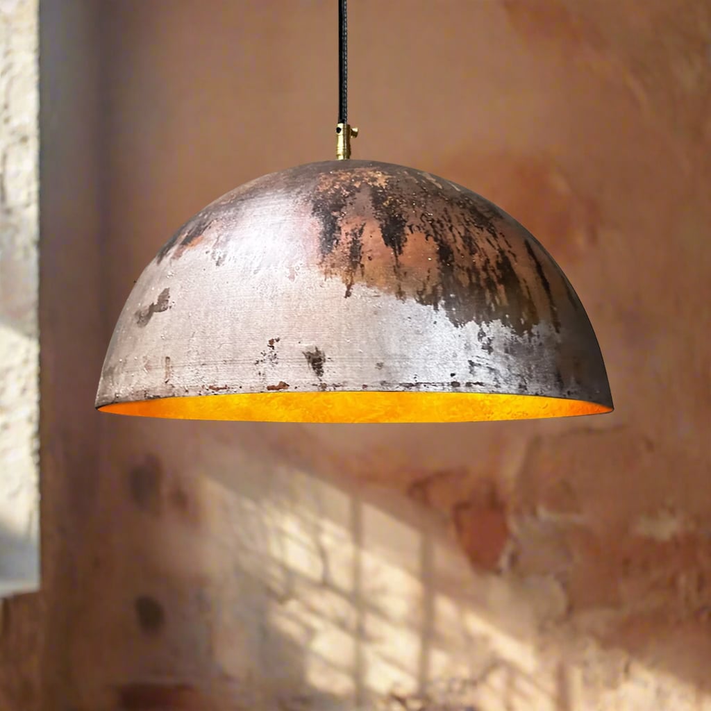 Oxidized copper dome pendant light with brushed golden interior, suspended in a sunlit room with textured terracotta walls