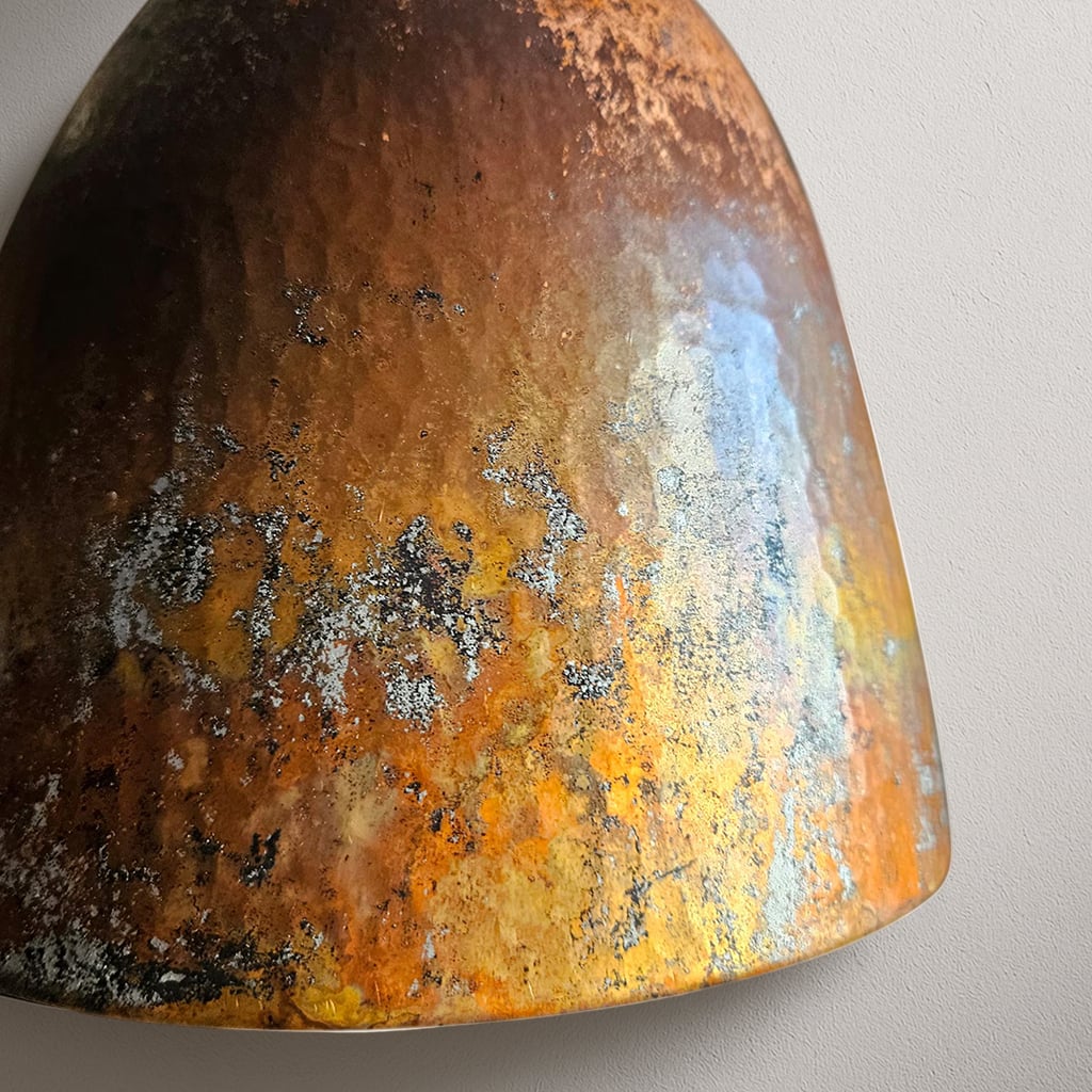 Close-up of a hand-hammered Moroccan pendant light with a richly oxidized copper surface featuring shades of rust, yellow, orange, and blue patina