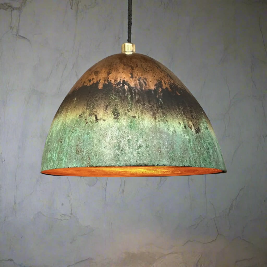 Oxidized green and copper hanging dome light with warm inner glow, set against a lightly textured plaster wall