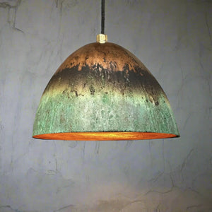 Oxidized green and copper hanging dome light with warm inner glow, set against a lightly textured plaster wall
