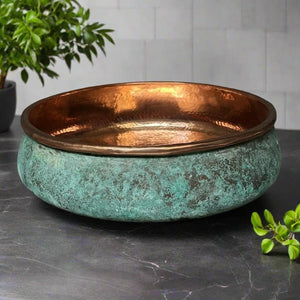 Elegant bathroom sink with a textured green patina exterior and hammered copper interior, placed on a dark stone surface