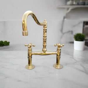 Polished brass bridge kitchen faucet with classic cross handles and a sculpted column-style spout, installed on a marble countertop