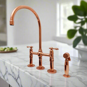 Polished copper bridge kitchen faucet with side sprayer installed on white marble countertop in a bright modern kitchen