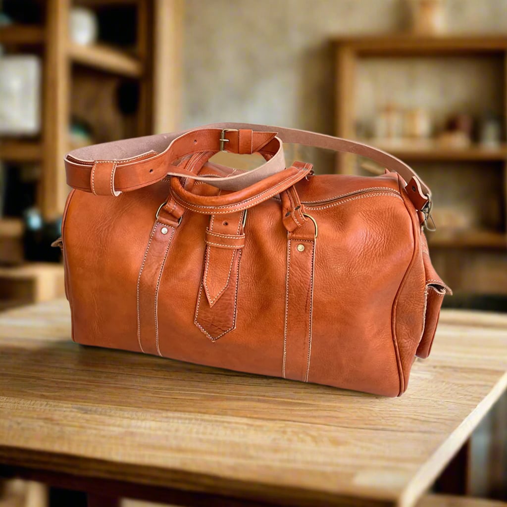 A premium tan leather duffle bag with adjustable shoulder strap, sturdy handles, and a sleek design. It features a spacious interior and side pocket for essentials, displayed on a wooden table in a cozy, warmly lit interior