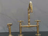 Thumbnail image of a video of a brass bridge faucet with lever handles and sprayer, displayed against a white textured wall and black countertop