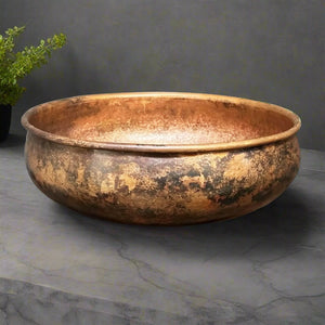 Handcrafted round antique patina copper sink with a wide rim and textured finish on a gray stone countertop