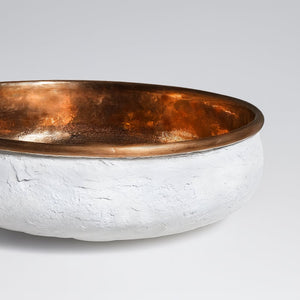 Close-up of a round basin with a hammered copper interior and textured white exterior, showcasing artisanal craftsmanship and modern elegance