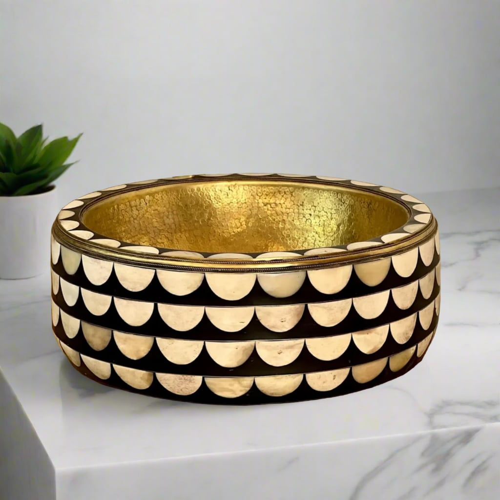 Side view of a luxurious round brass sink with elegant mother-of-pearl half-moon pattern inlay and hammered gold interior, placed on a marble counter
