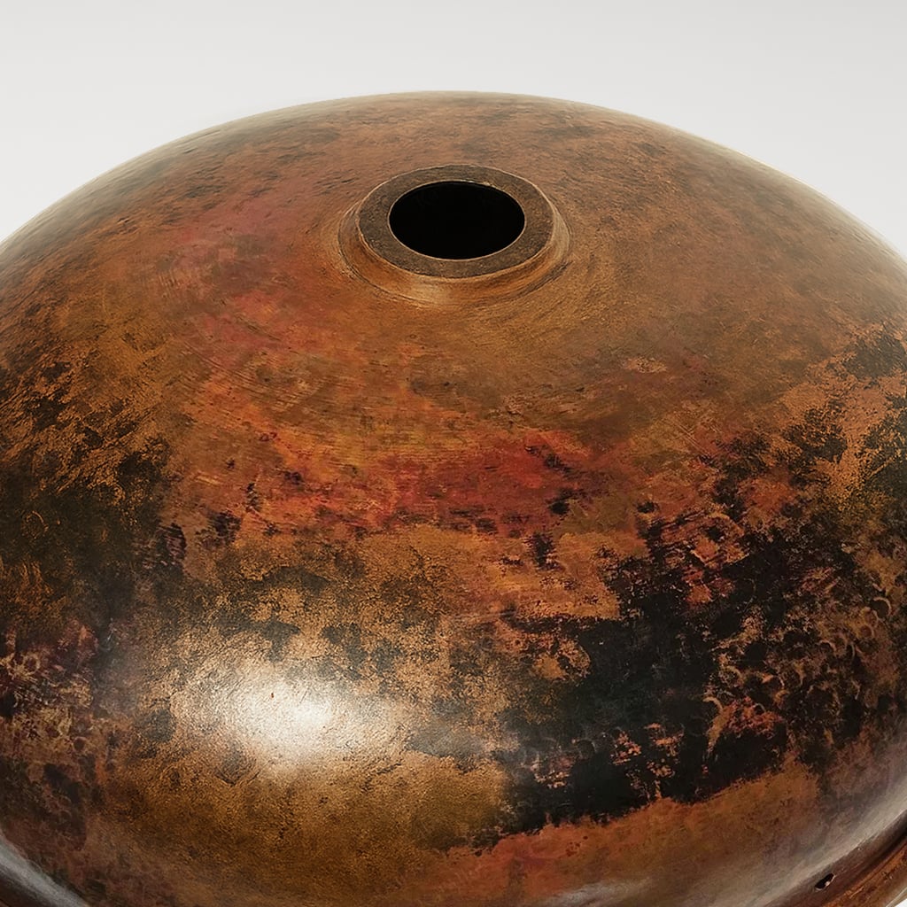 Underside view of a round copper sink with drain hole, featuring a rich brown patina with natural dark and reddish variations