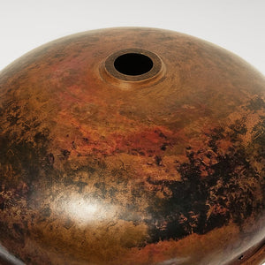 Underside view of a round copper sink with drain hole, featuring a rich brown patina with natural dark and reddish variations