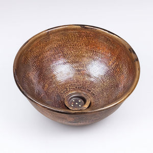 Handcrafted round copper sink with a hammered texture and antique patina, featuring a central drain for a rustic yet refined bathroom design