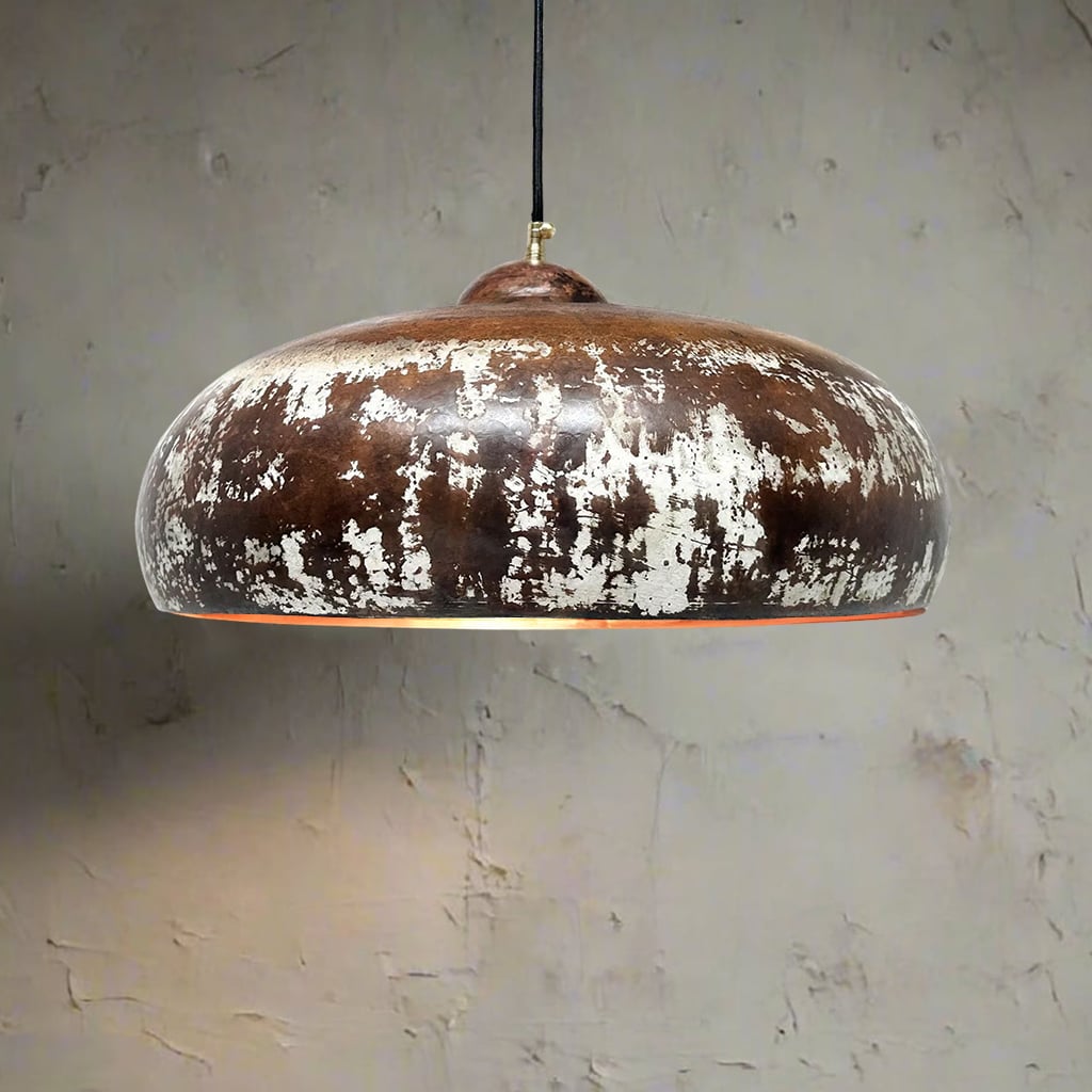 Dome-shaped pendant light with a distressed brown and white patina, hanging above a cabinet with decor elements in a softly lit room.