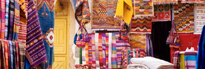 Colorful Moroccan textiles, rugs, and woven bags displayed at a vibrant street market, showcasing traditional patterns and rich craftsmanship