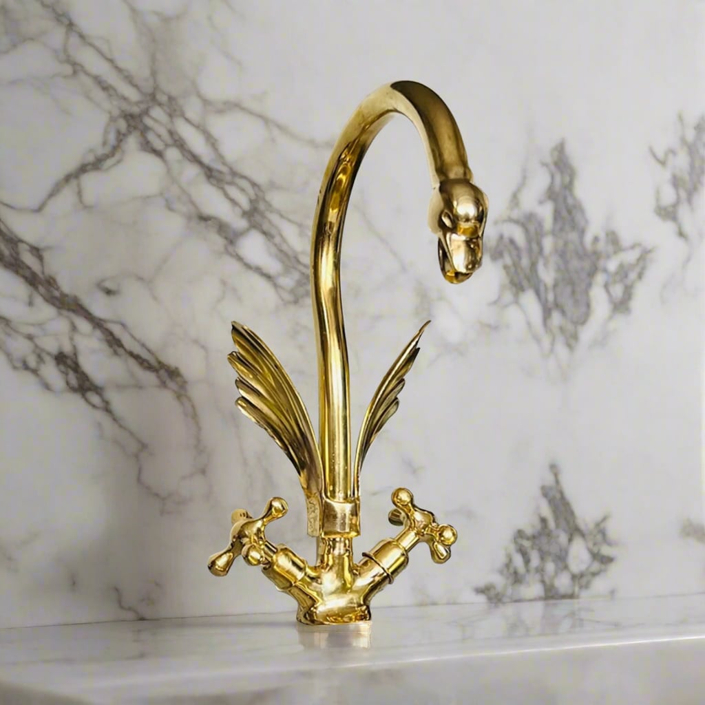 Ornate brass swan-neck faucet with feather detailing and traditional knob handles placed over a marble countertop