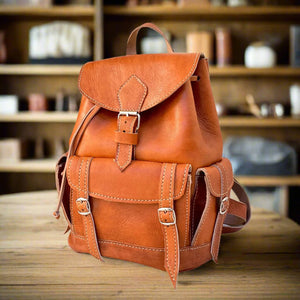 Side view of a tan leather backpack highlighting its functional design, including buckle closures and spacious compartments, set on a rustic wooden table