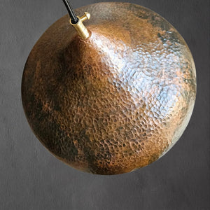 Top view of a hand-hammered copper dome pendant lamp, showing detailed texture and brass hardware connection with hanging cord