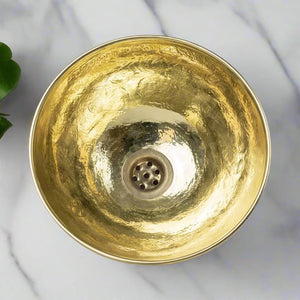 Top view of a hand-hammered brass bathroom sink with engraved floral patterns on a marble counter