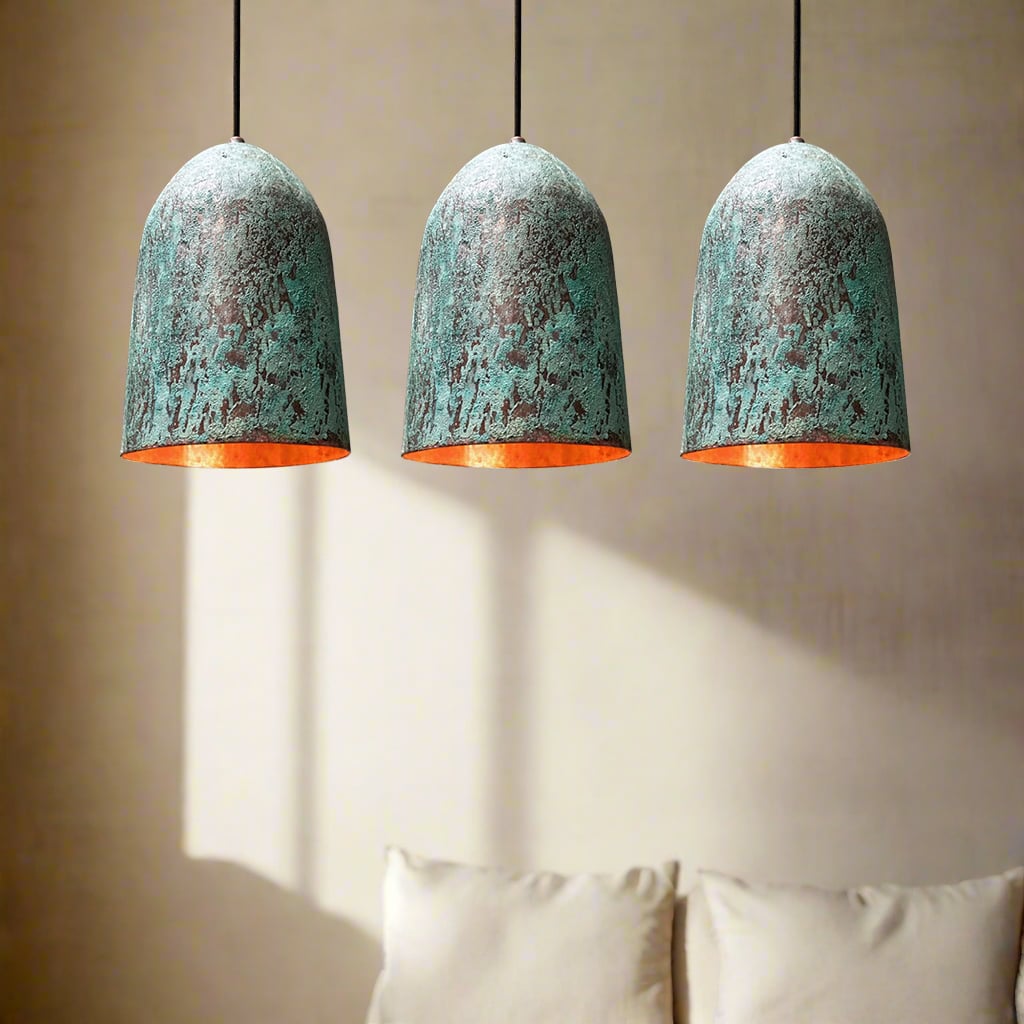 Three green patina copper pendant lights with warm glowing interiors hanging over a light-toned seating area.
