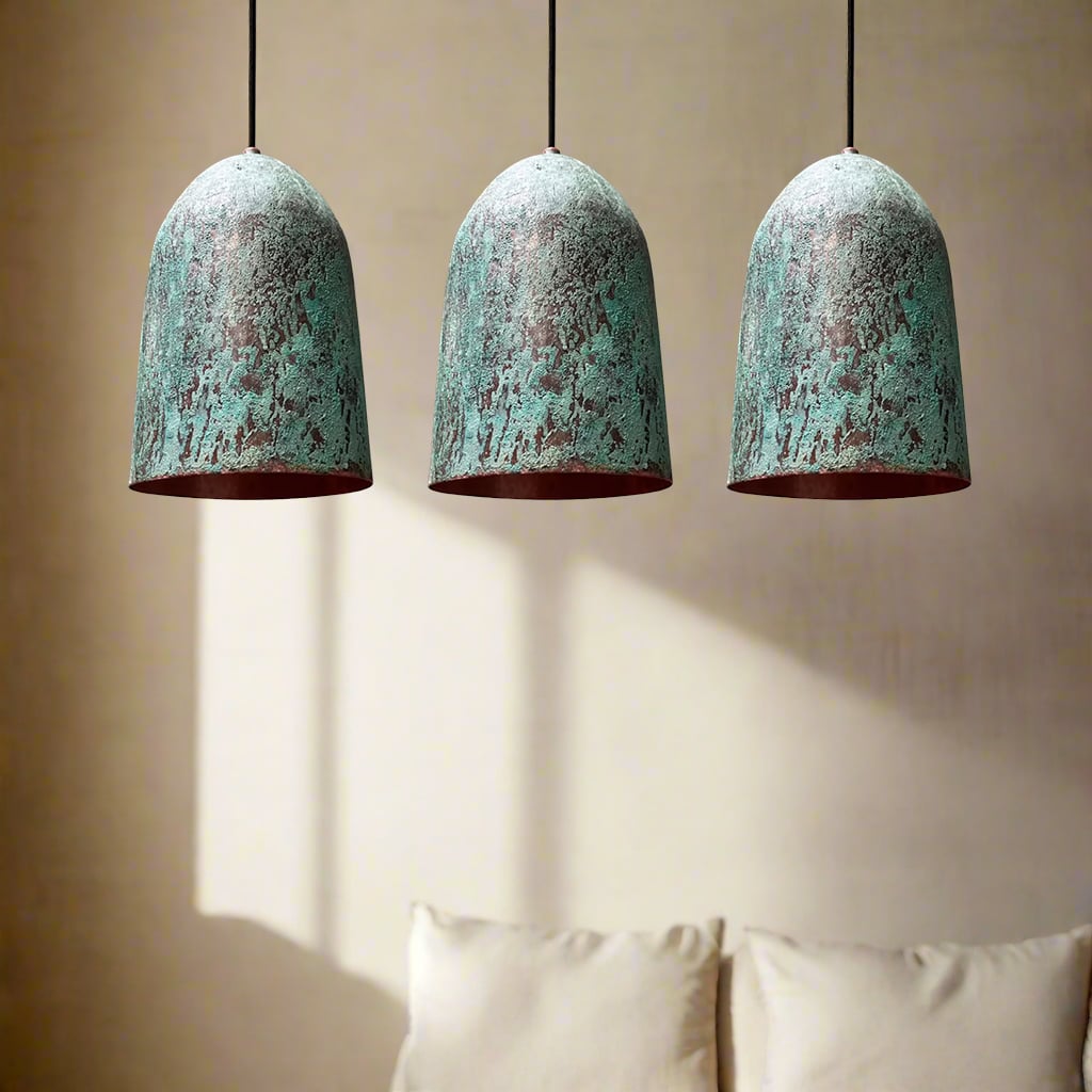 Set of three green patina copper pendant lights casting subtle shadows on a beige wall above a cozy couch.