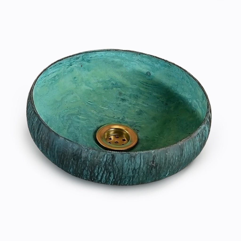 Round turquoise bathroom sink with textured exterior and brass drain against a light background