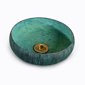 Round turquoise bathroom sink with textured exterior and brass drain against a light background