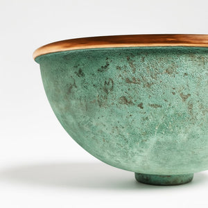 Close-up of a round copper basin with a green verdigris patina exterior and polished copper rim, showcasing artisanal texture and craftsmanship.